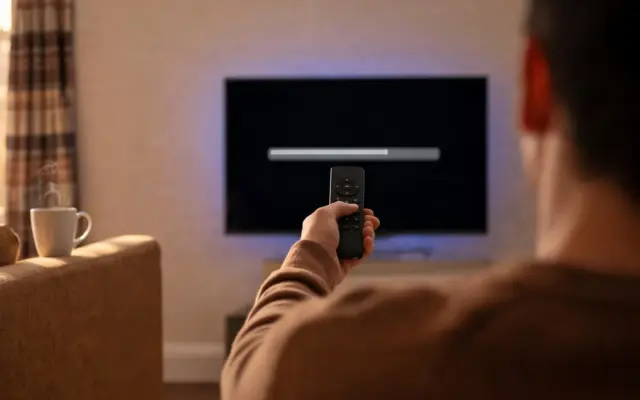 A viewer pointing a streaming-stick remote at a TV showing a download progress bar